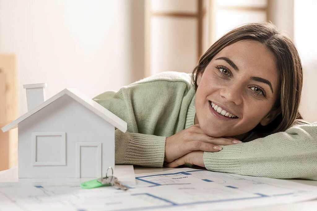 mulher ao lado de miniatura de casa, planejando investir em imóveis